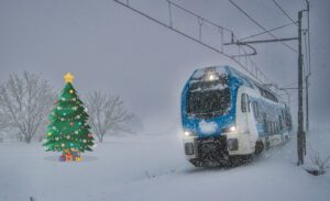 Vlak Stadler v snegu in božično drevesce ob progi.